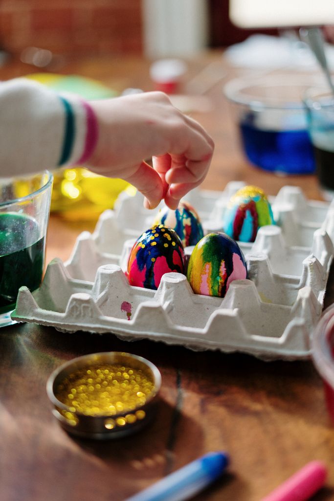 Hand decorating vibrant Easter eggs with paint and glitter, perfect for festive crafts.